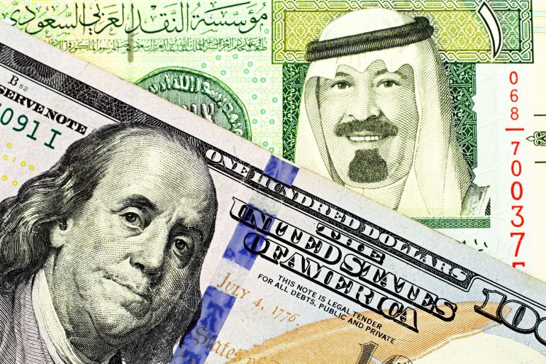 A close up image of a blue American one hundred dollar bill and a Saudi Arabian one riyal note